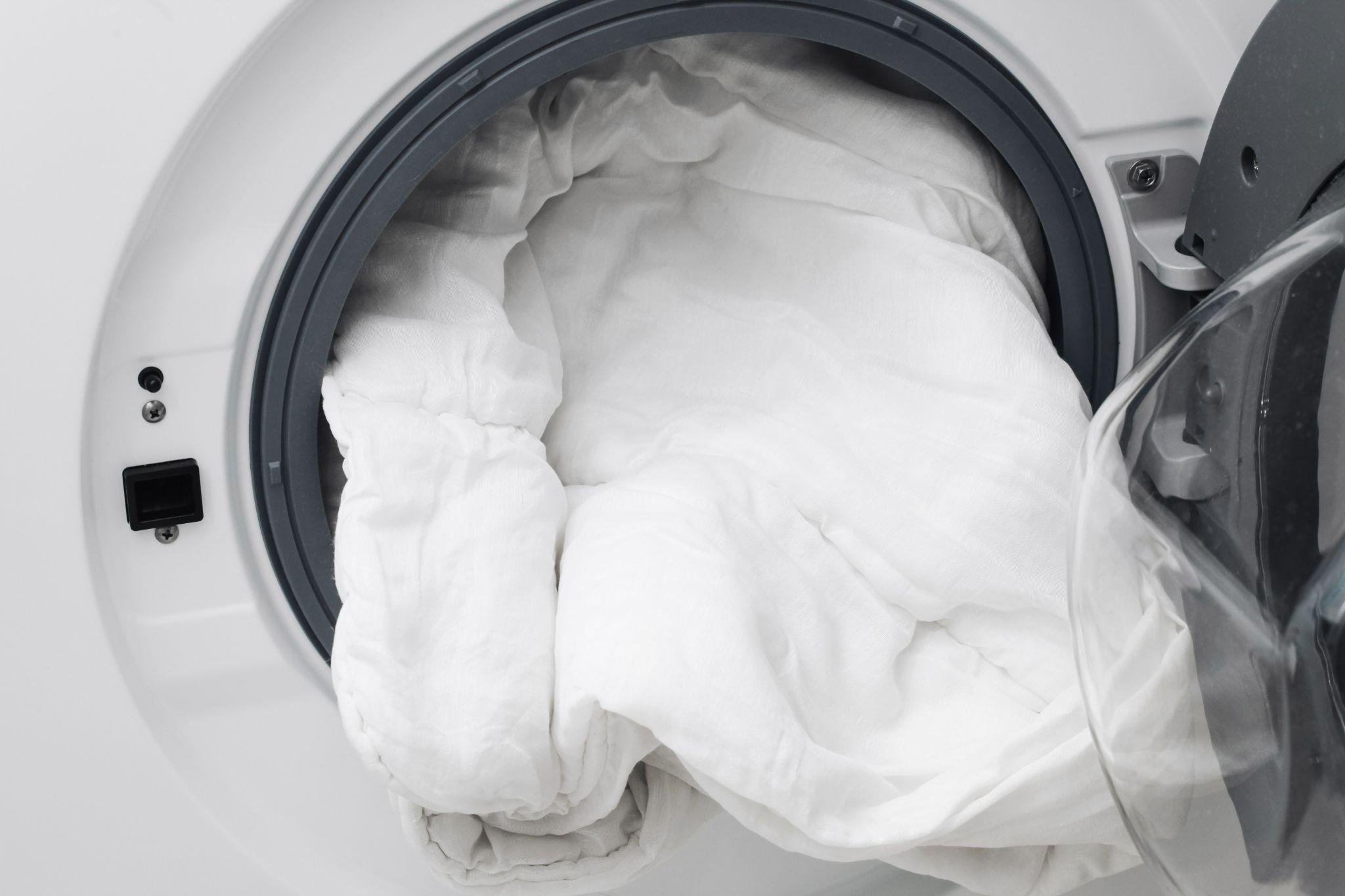 A white comforter being loaded into a large capacity front loading washing machine