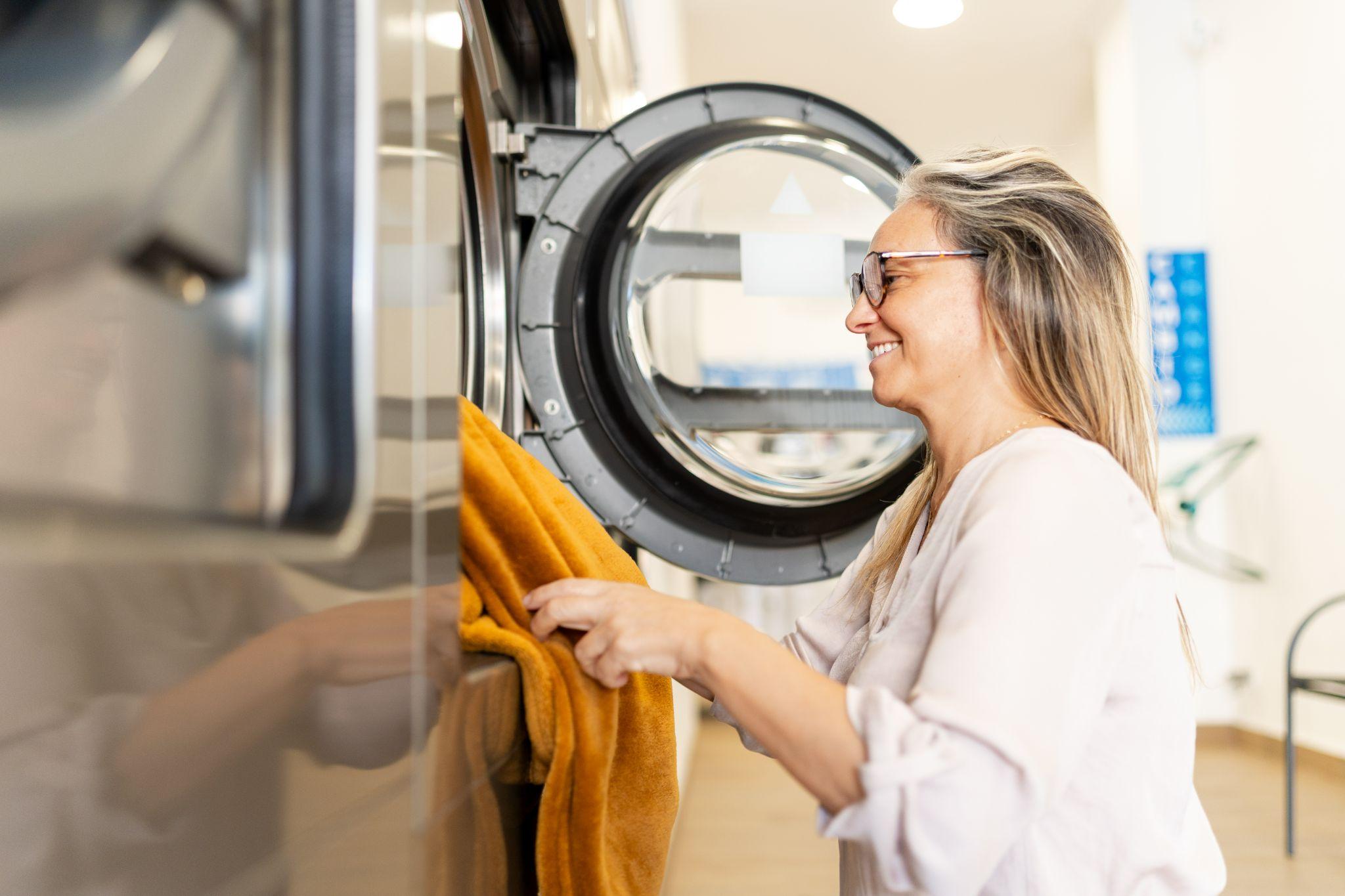 Laundry tips and tricks to save time and get better results 1 A woman loading a blanket into a large laundromat washing machine